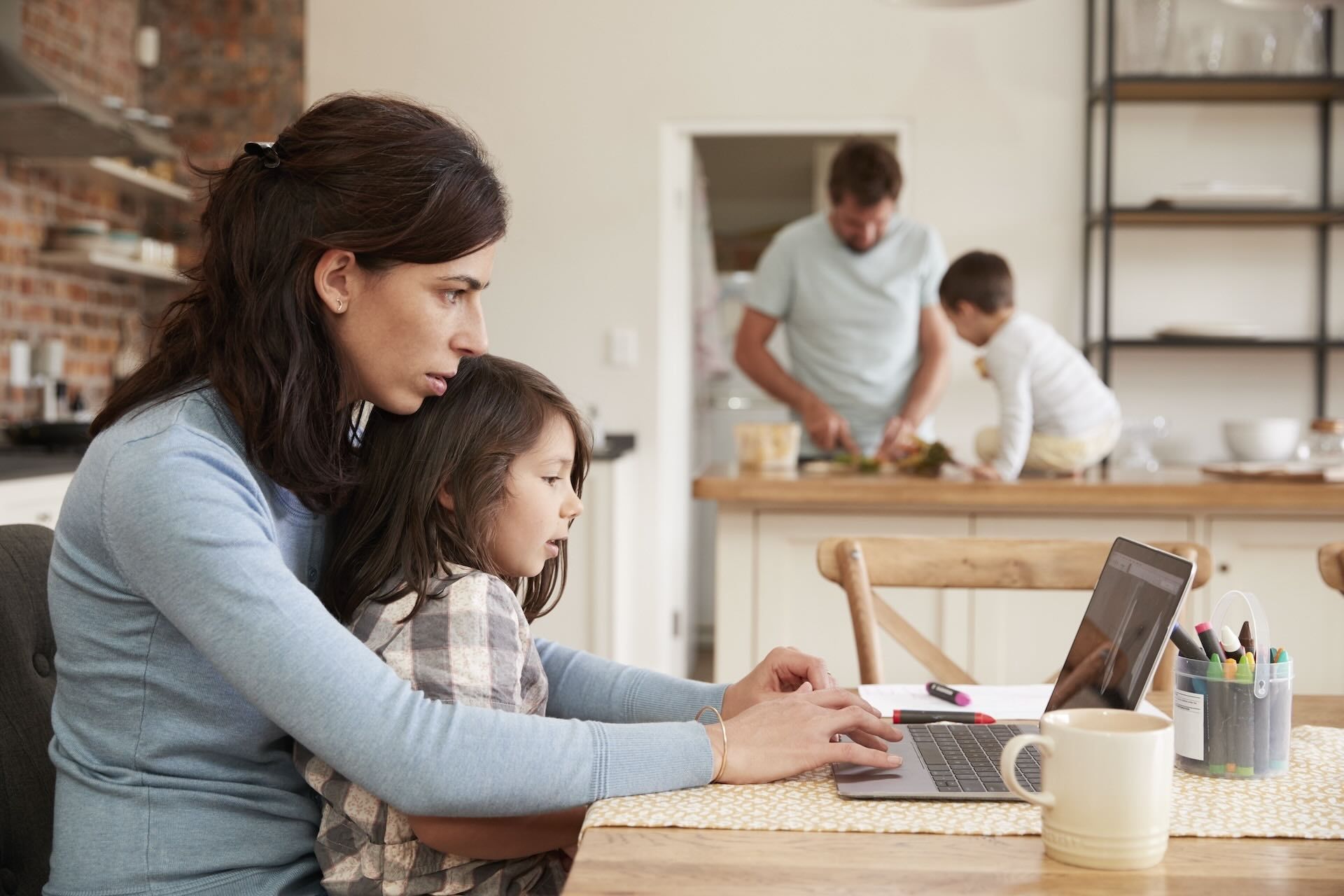 Busy Family Home With Mother Working As Father Prepares Meal